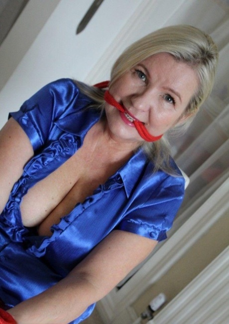 Older blonde is gagged and tied up in a variety of outfits inside her house